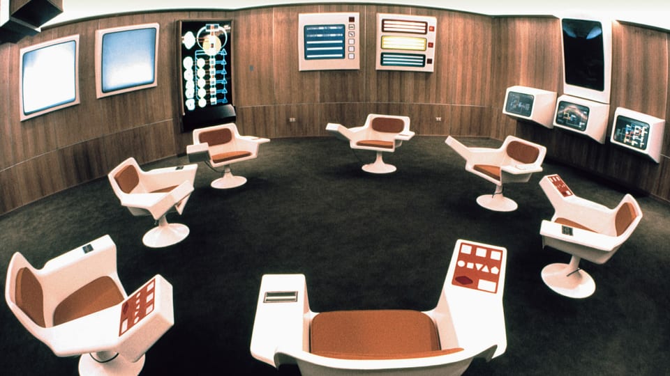 ein Raum mit futuristischen Bildschirmen und Sesseln