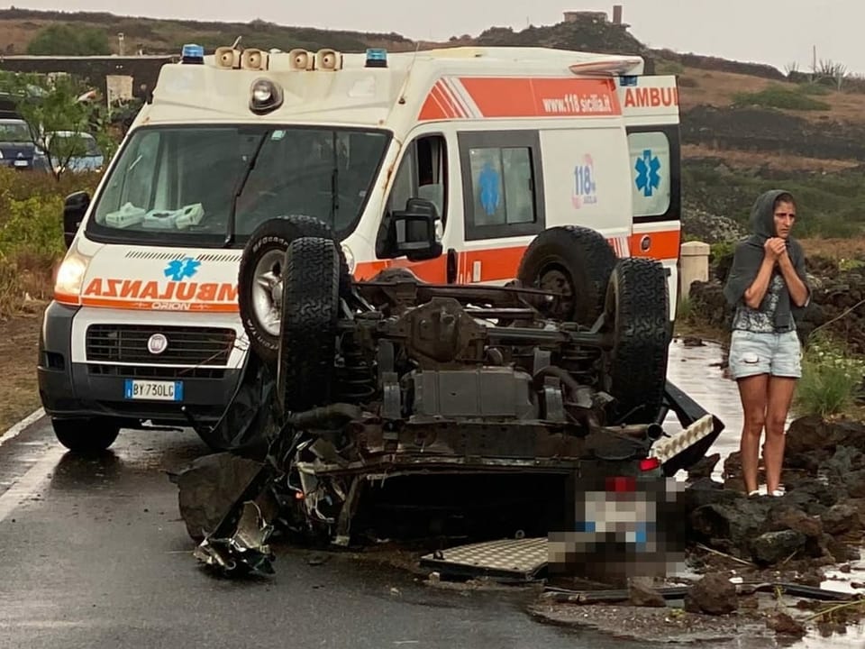Eine Frau und ein zerstörter Wagen stehen vor einem Krankenwagen
