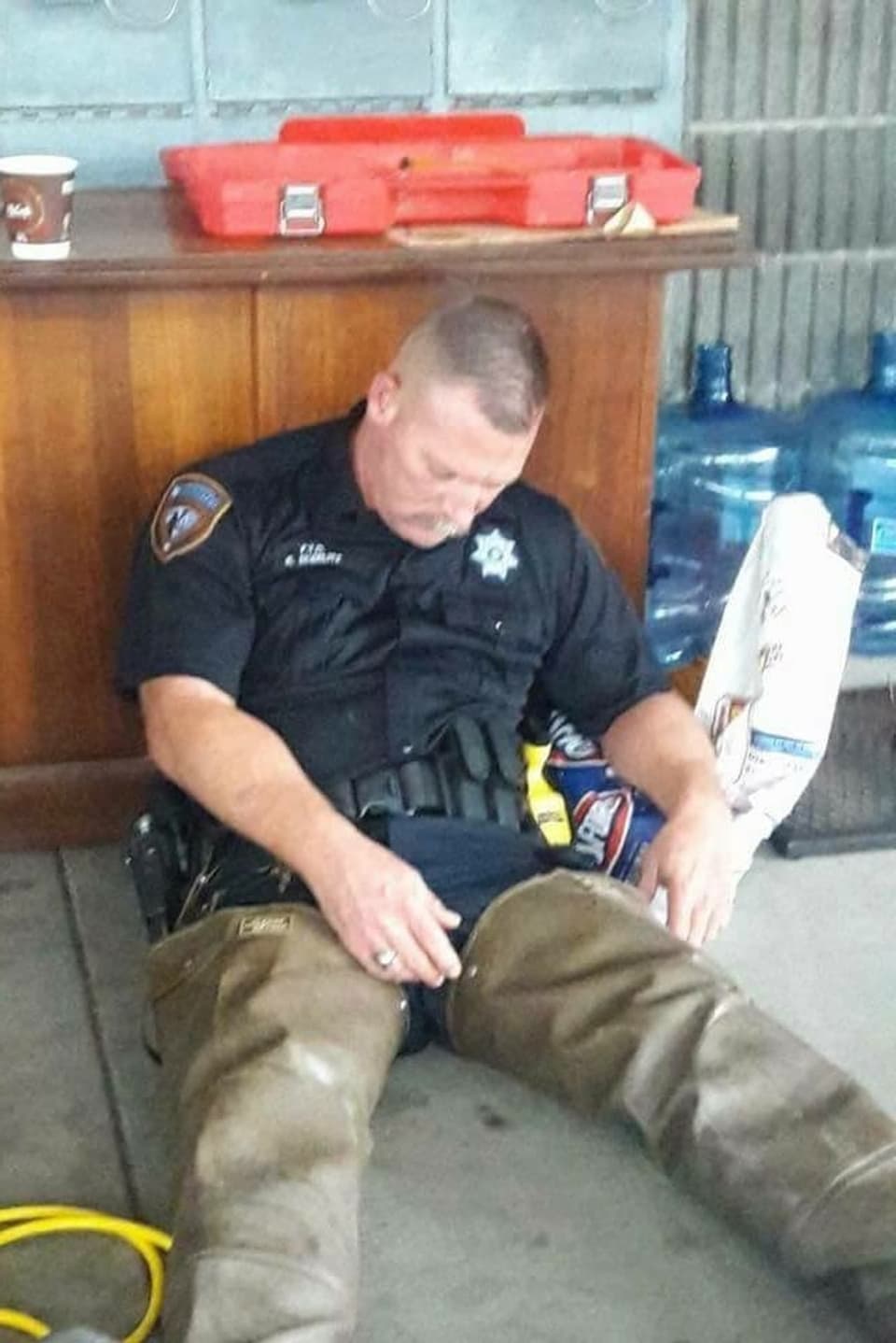 Ein Polizist schläft auf dem Fussboden sitzend.