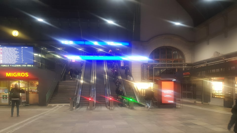 Leere Halle im Bahnhof Basel, Menschen auf der Rolltreppe.
