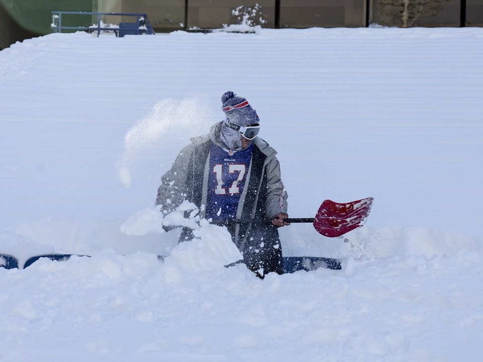 Ein Fan der Buffalo Bills schaufelt Schnee von den Plätzen im Stadion.