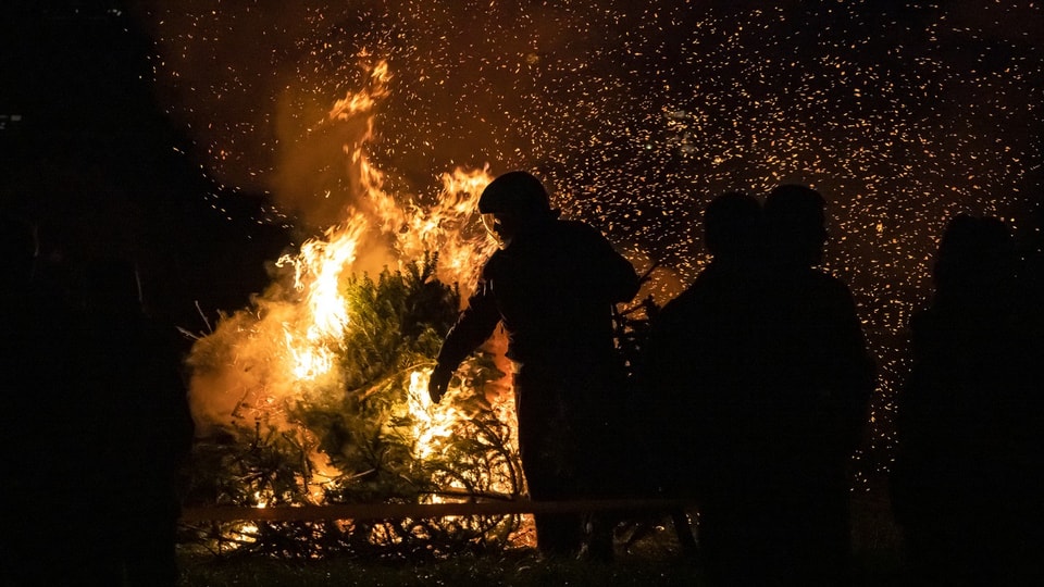 Ein Mann in Uniform steht vor einem brennenden Haufen von Bäumen.