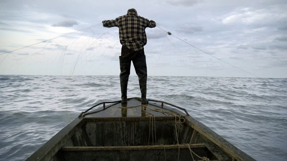 Foto Mann mit Rücken zugewandt steht auf kleinem Holzboot, hält Fischernetz