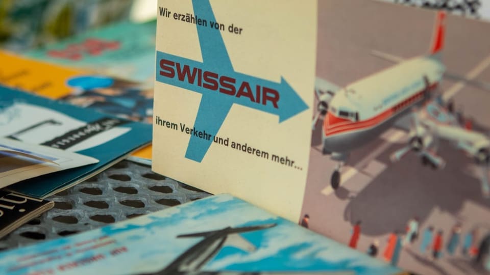 Alte Prospekte: Weisse Karte mit blauem Flugzeug-Symbol.