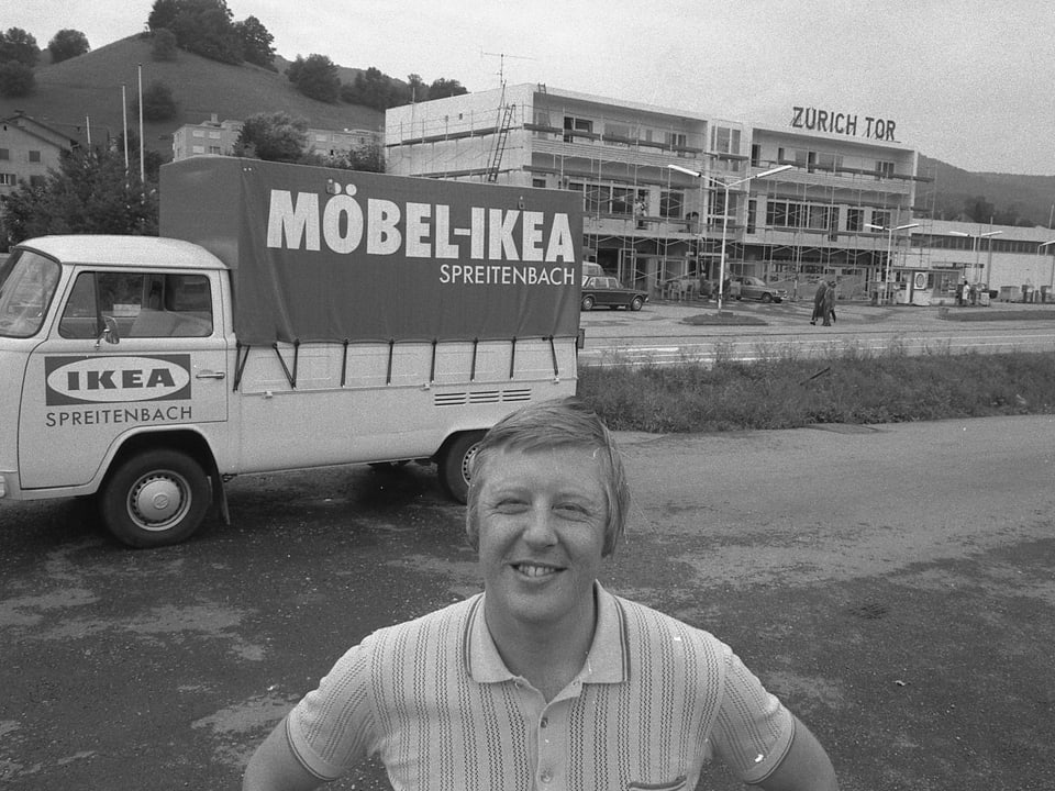 Ein Mann steht vor einem Ikea-Transporter und dem Möbelhaus.