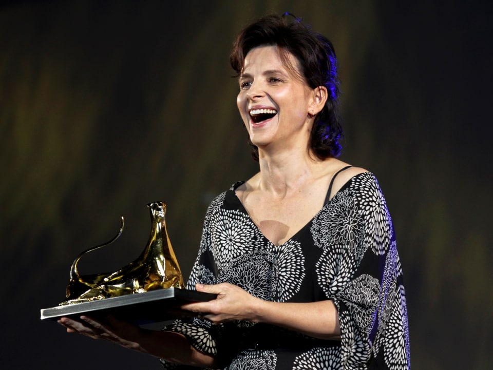 Juliette Binoche lacht und hält den «Excellence Award Moët & Chandon»-Award.