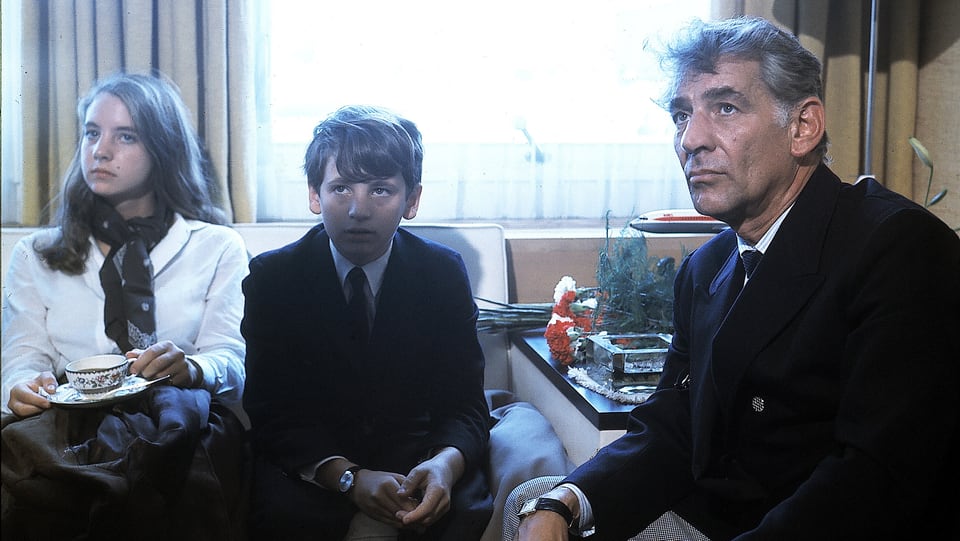 Leonard Bernstein und seine zwei Kindern sitzen auf Sofas.