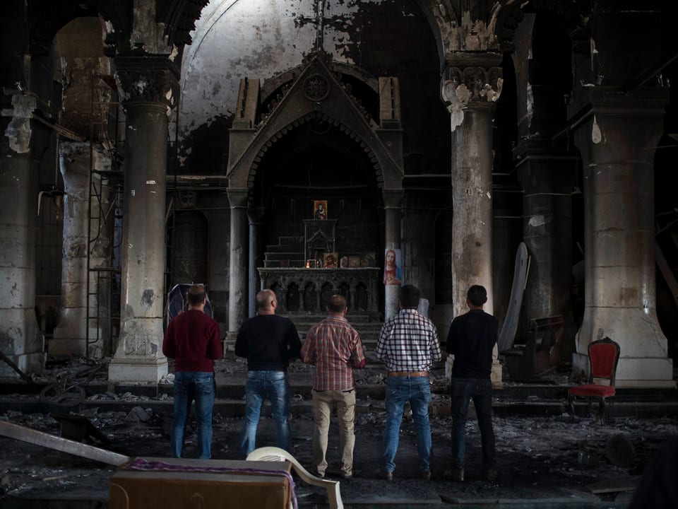 Menschen betrachten die zerstörte Kirche in Karakosch. 