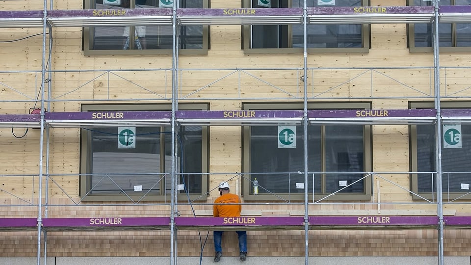 Ein Bauarbeiter sitzt auf einem Baugerüst.