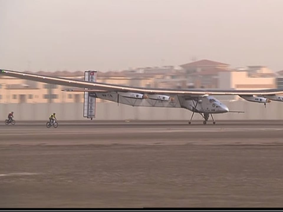 Startendes Solarflugzeug mit grosser Spannweite vor sandfarbenen Häusern