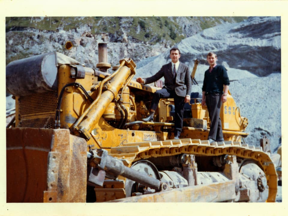 Ein Arbeiter und ein Mann im Anzug posieren auf einer Baumaschine.