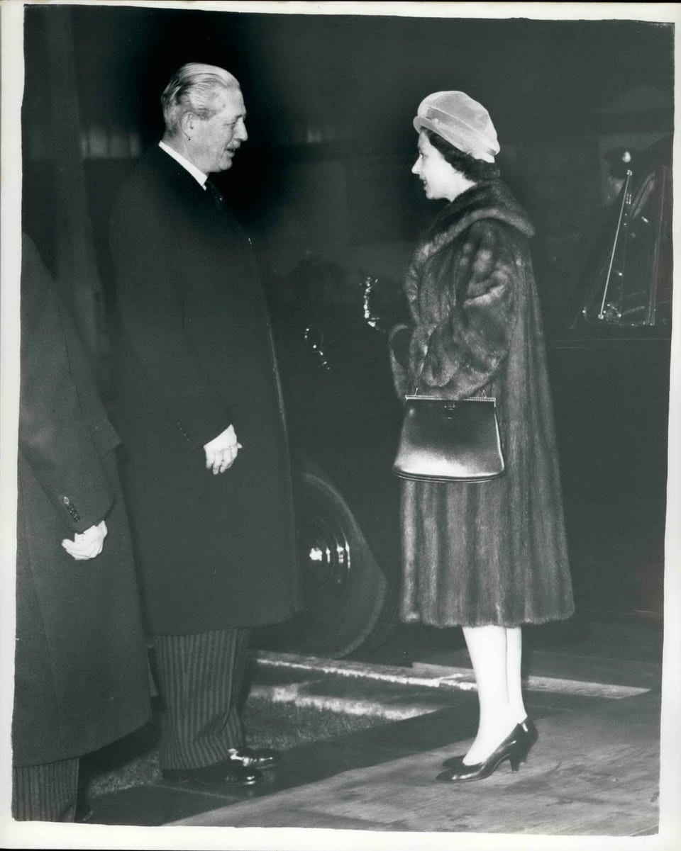 Foto in schwarz-weiss. Mann und Frau mit langen Mänteln schauen sich an. Die Frau trägt eine Mütze.