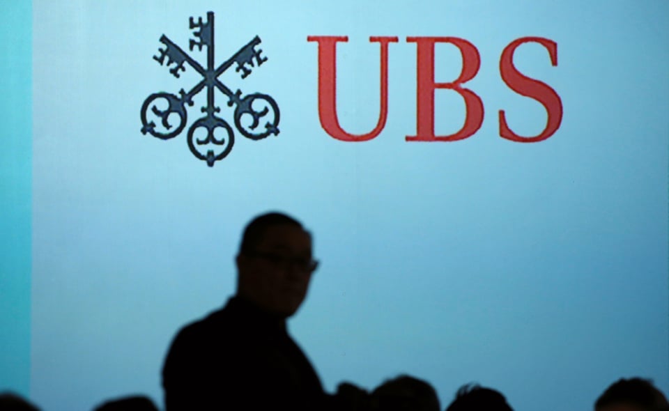 Symbolbild: UBS-Logo an der Wand, davor Personensilhouetten.