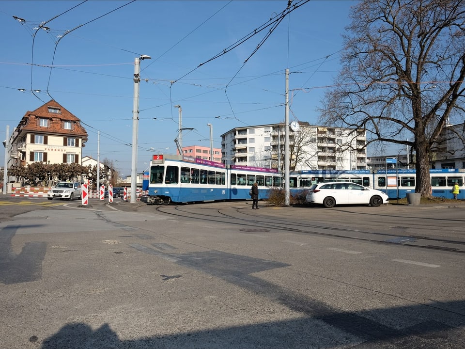 Ein blau-weisses Tram an der Endstation mit einem Baum und einer Baustelle.