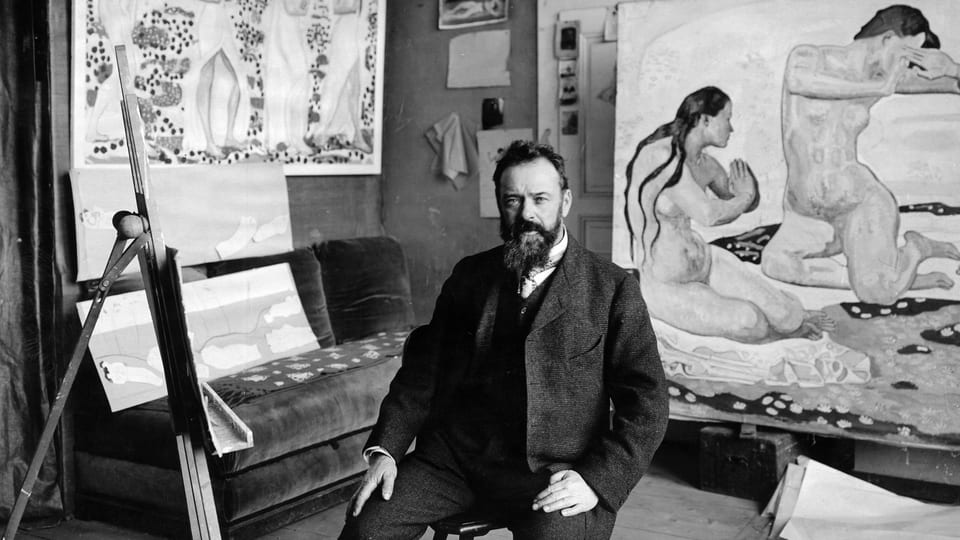 Ein Mann sitzt in seinem Atelier, umringt von Bildern