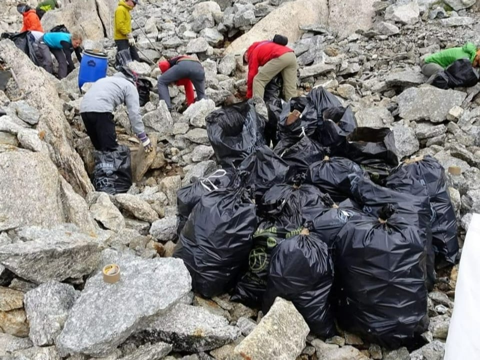 Menschen sammeln Müll auf zwischen Geröll und packen ihn in Abfallsäcke.