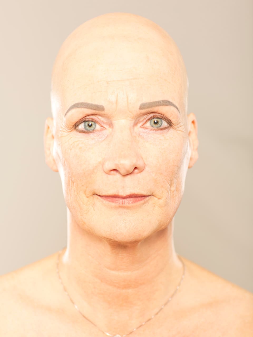 Porträt: Nahaufnahme einer Frau mit Glatze vor grauem Hintergrund.