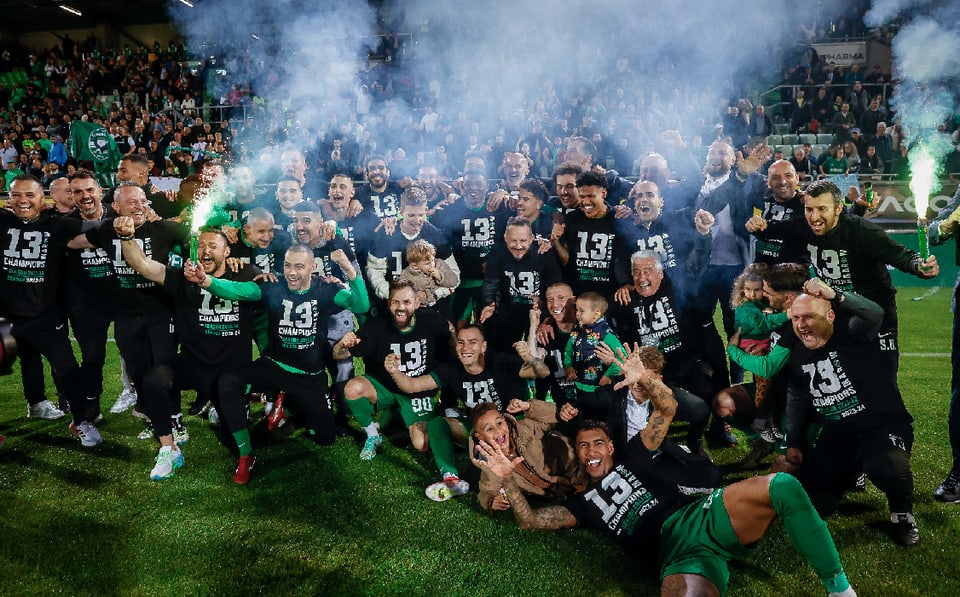 Fussballmannschaft feiert Sieg mit grünen Rauchfackeln auf dem Spielfeld.