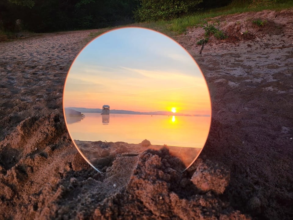 Sonnenaufgang in einem Spiegel der im Sand steckt