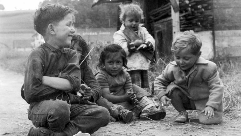 Ein Gruppe von etwas verwahrlosten Kindern sitzt lachend auf der Strasse.