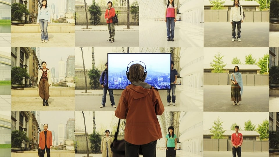 Person steht mit Kopfhörer vor Bildschirm und Fotografien