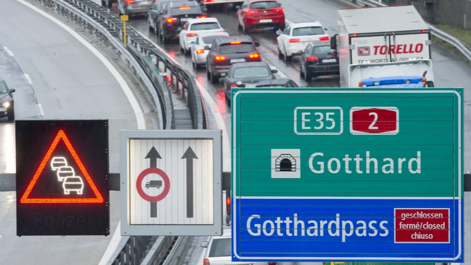 Autokolonne von oben aufgenommen, im Vordergrund Anzeigetafel mit Hinweis auf den Gotthardtunnel und Gotthardpasss sowie Stauwarnung