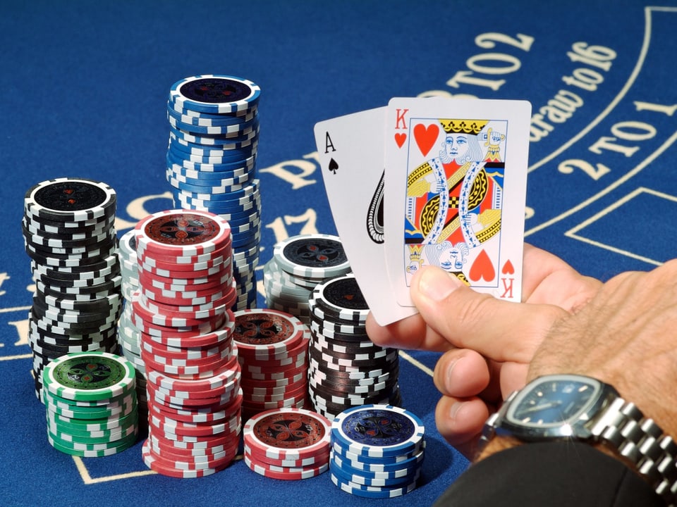 Eine Männerhand hält zwei Karten in der Halt und spielt erfolgreich Black Jack.
