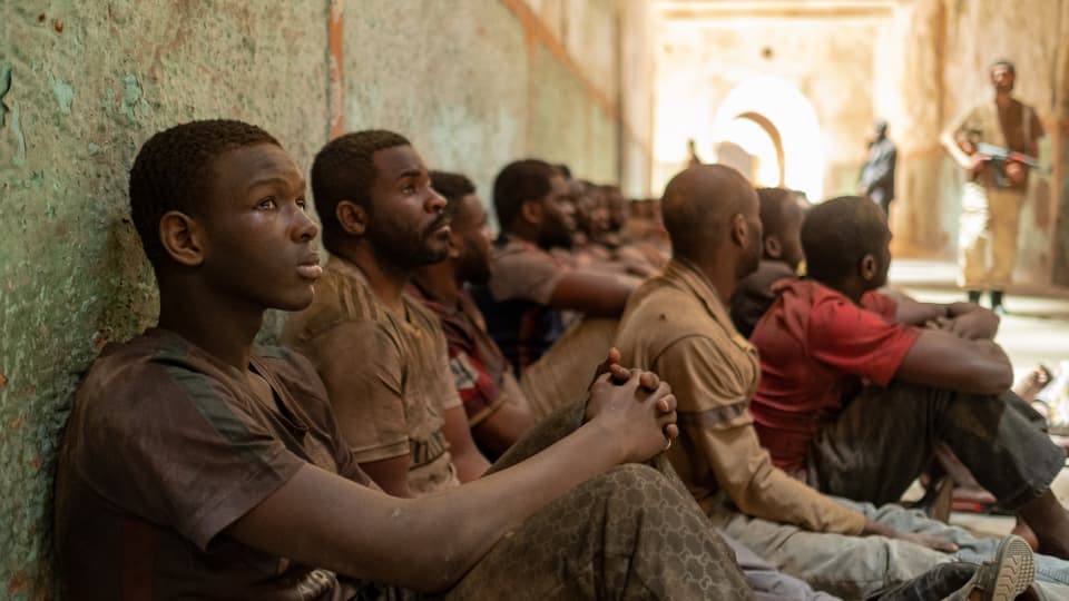 Mehrere Gefangene sitzen in einem Internierungslager am Boden. 