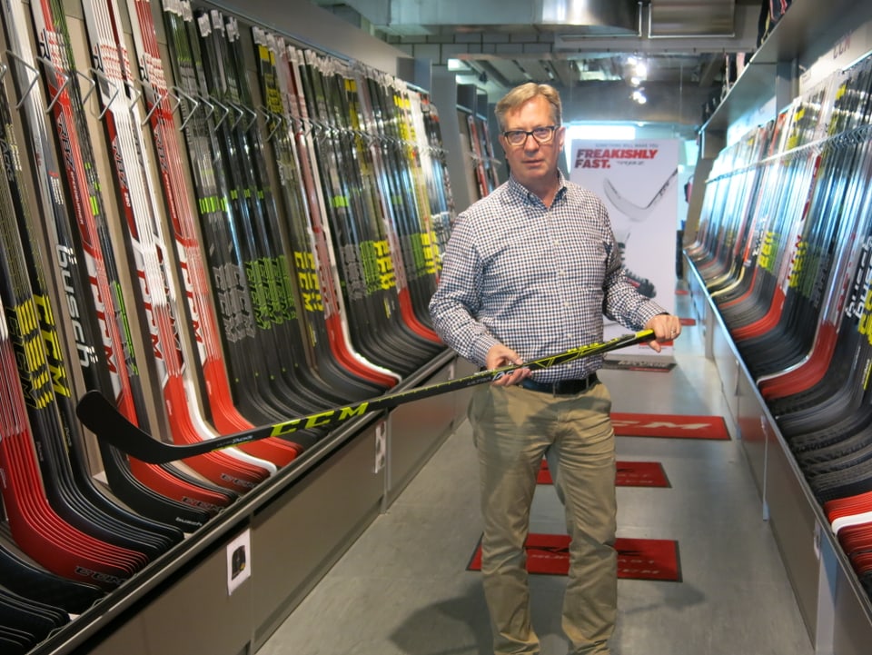 Firmenchef Roland Gerber umgeben von Eishockey-Stöcken.