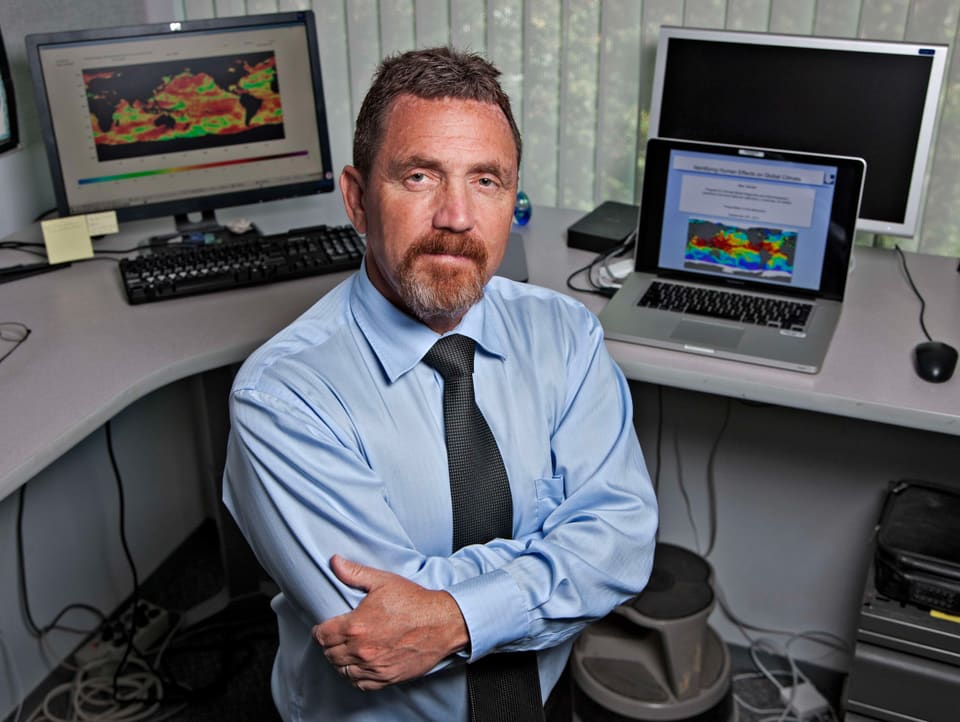 Mann mit verschräönten Armen vor Monitoren mit Klimadaten