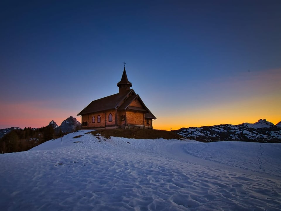 Kirche auf Schneewiese. Schön gefärbter Himmel im Hintergrund.
