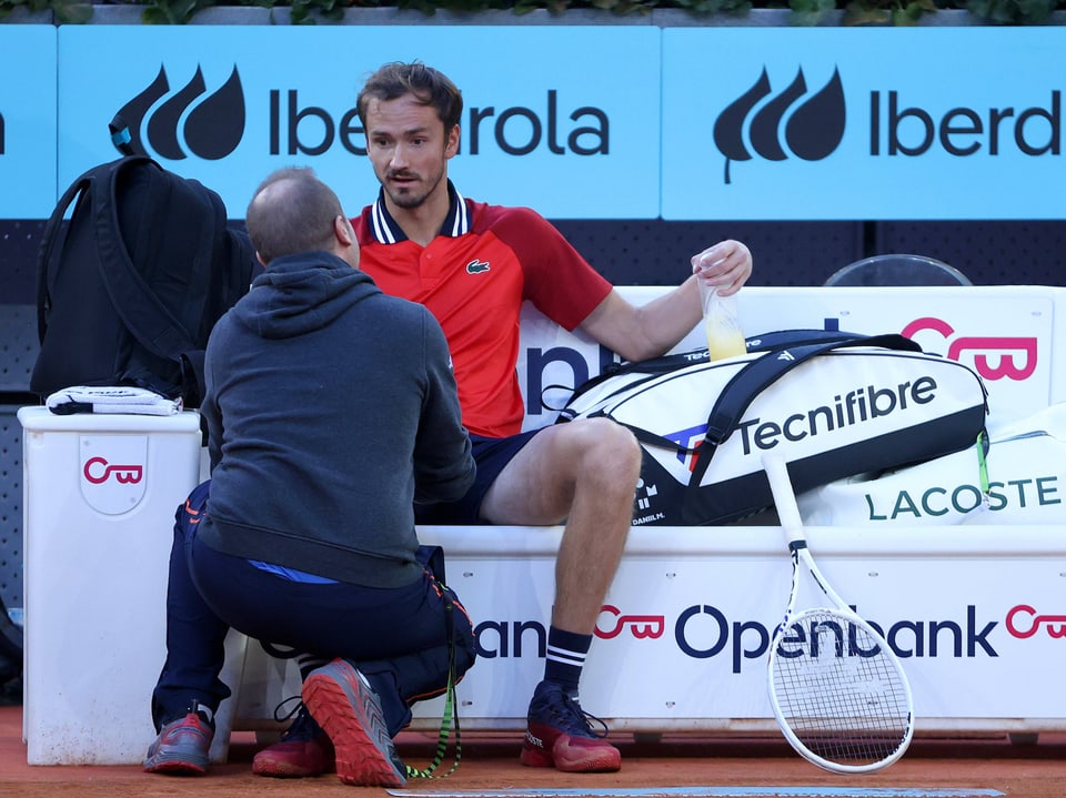 Tennisspieler sitzt während einer Pause und unterhält sich mit einem Trainer auf dem Tennisplatz.