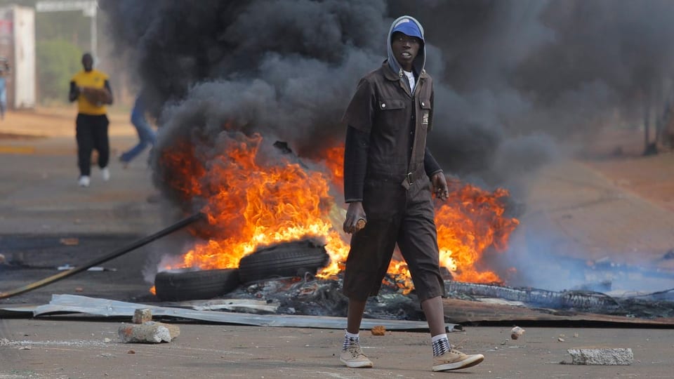 Ein junger Mann mit einem Stein in der Hand geht an einer brennenden Barrikade vorbei.