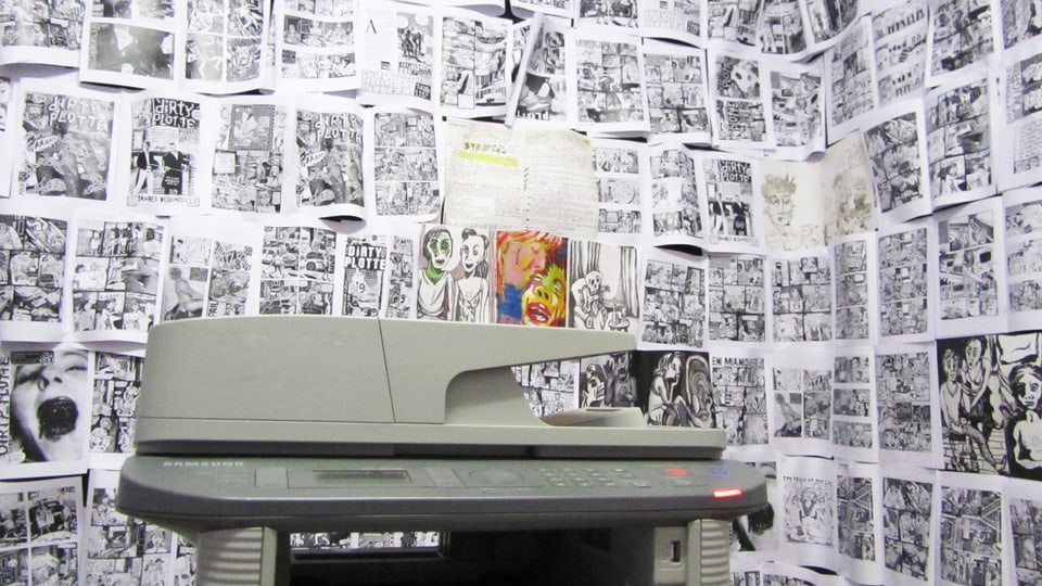 Kopiergerät vor einer Wand mit kopierten Comics. 