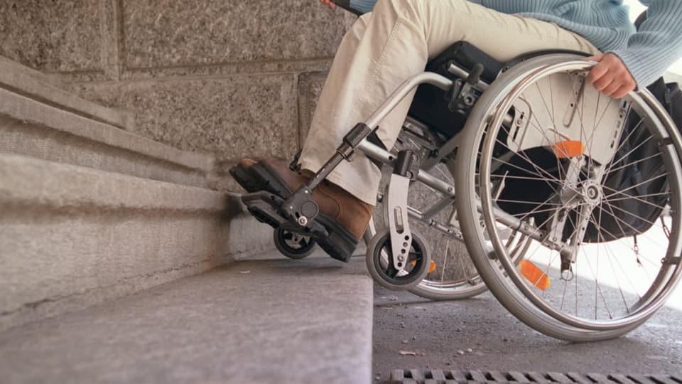 Eine Frau im Rollstuhl steht unten an einer Treppepe