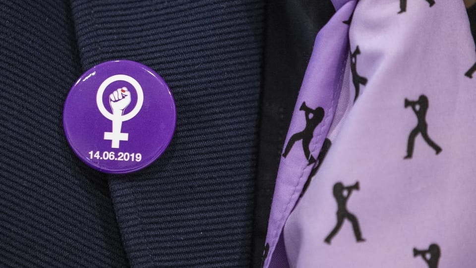 Violetter Button mit gereckter Faust und dem Zeichen für das weibliche Geschlecht.