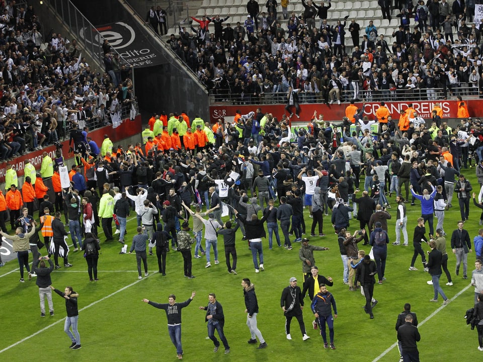 Fans stürmen freudig das Spielfeld und jubeln mit den Spielern von Amiens.