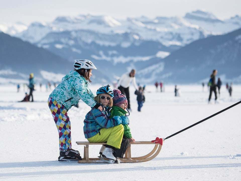 Kinder mit Schlittschuhen und Schlitten auf dem gefrorenen Sihlsee bei Einsiedeln.