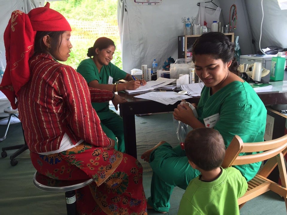 Zwei Mitarbeiterinnen des Roten Kreuzes sitzen mit einer Patientin an einem Tisch