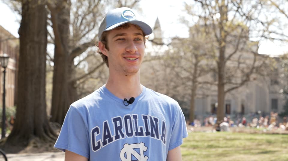 Junger weisser Mann mit Uni-Carolina-Shirt schaut an Kamera vorbei