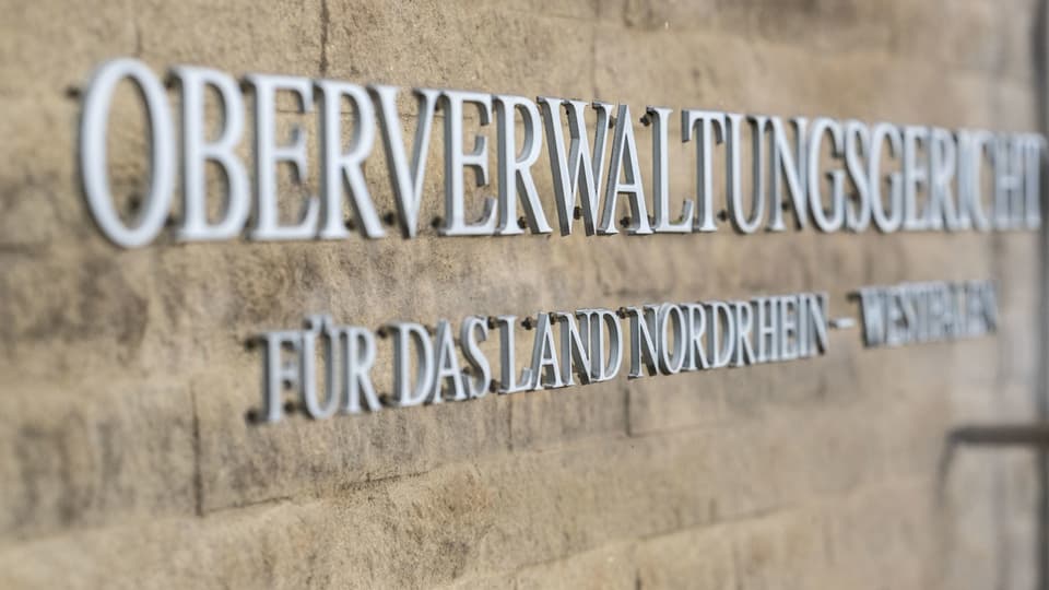 Schild 'Oberverwaltungsgericht für das Land Nordrhein-Westfalen' an einer Steinwand.