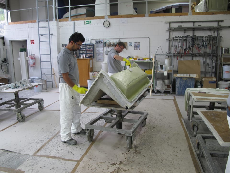 Zwei Mitarbeiter tragen Schicht für Schicht Kunststoff und Harz auf eine Holzform auf. 