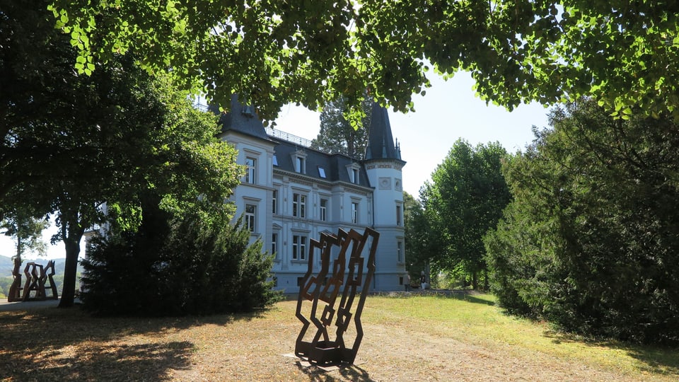 Skulptur aus Eisen auf einem Rasenfeld, dahinter grosse Villa