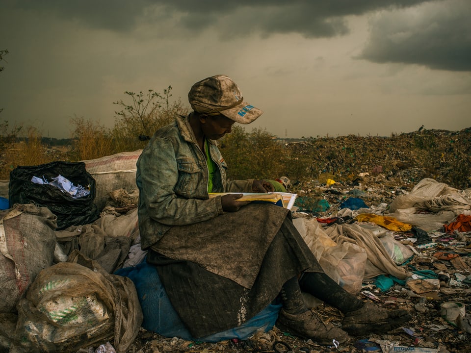 Eine Müll-Sammlerin aus Kenia liest ein Buch, das sie auf der Halde gefunden hat.