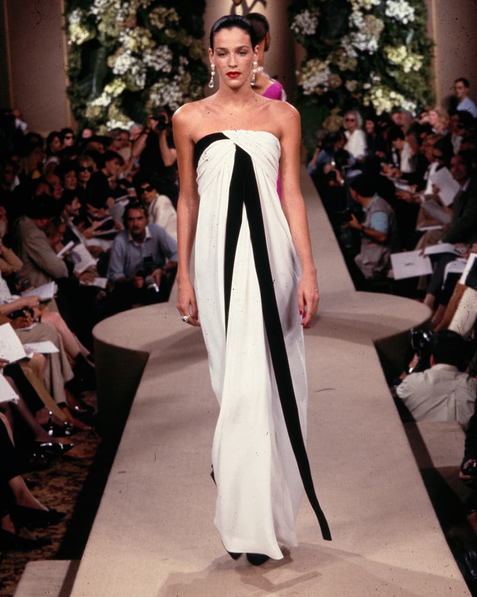 Woman on the catwalk in a white, floor-length dress with black, vertical stripes, flying freely like a loop.