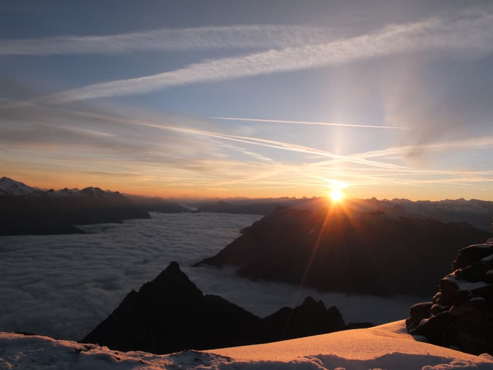 Blick ins nebelgeflutete Unterengadin. Am Horizont die gerade erst aufgegangene Sonne und die noch im Schatten liegenden Berge.