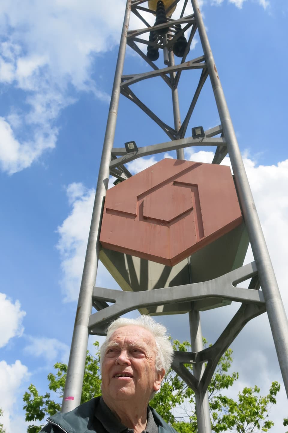 Der 90jährige Ernst Wermuth steht vor einem hohen Turm mit Glocken dran. 