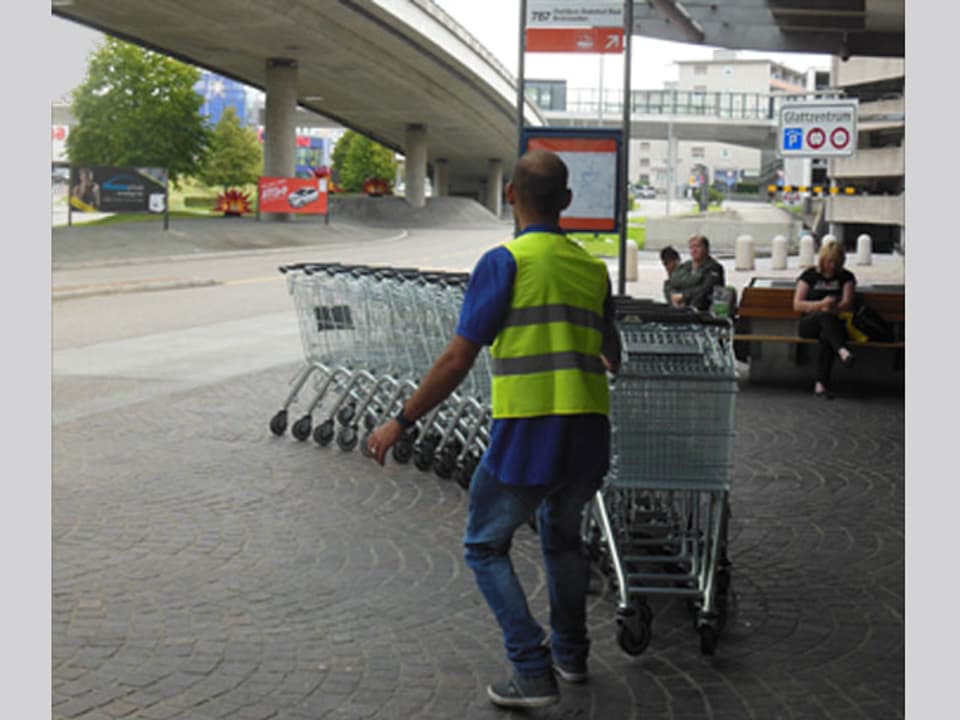 Ein Mann zieht eine Reihe ineinnader verschachtelte Einkaufswagen.