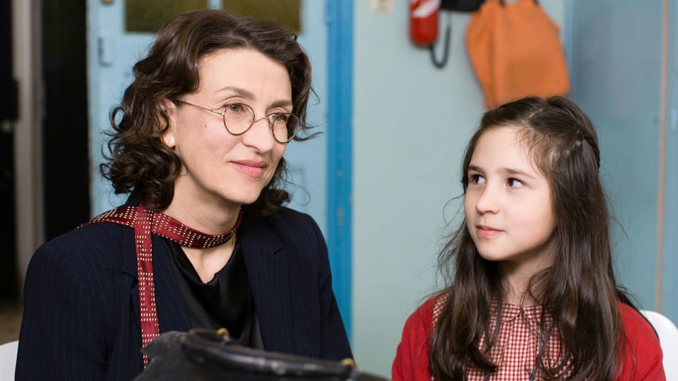 Frau mit Brille neben einem Mädchen in einem Schulzimmer