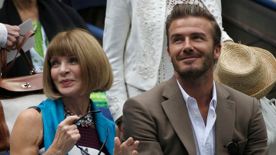Anna Wintour (links) und David Beckham (rechts) sitzen nebeneinander und lächeln.